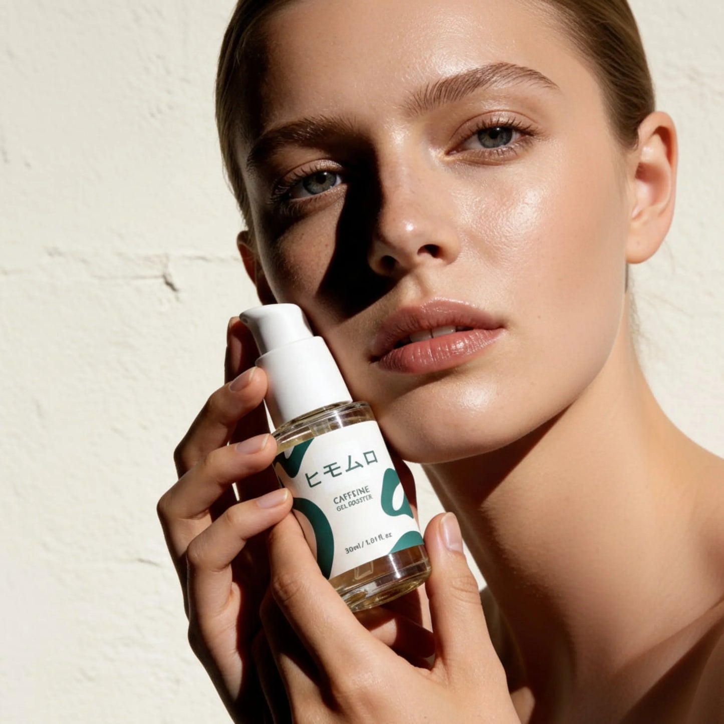 Kvinna med glödande hud håller en flaska Caffeine Gel Booster serum framför ansiktet