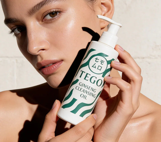Kvinna med glowy hud håller flaska Tego Ginseng Cleansing Oil nära ansiktet.