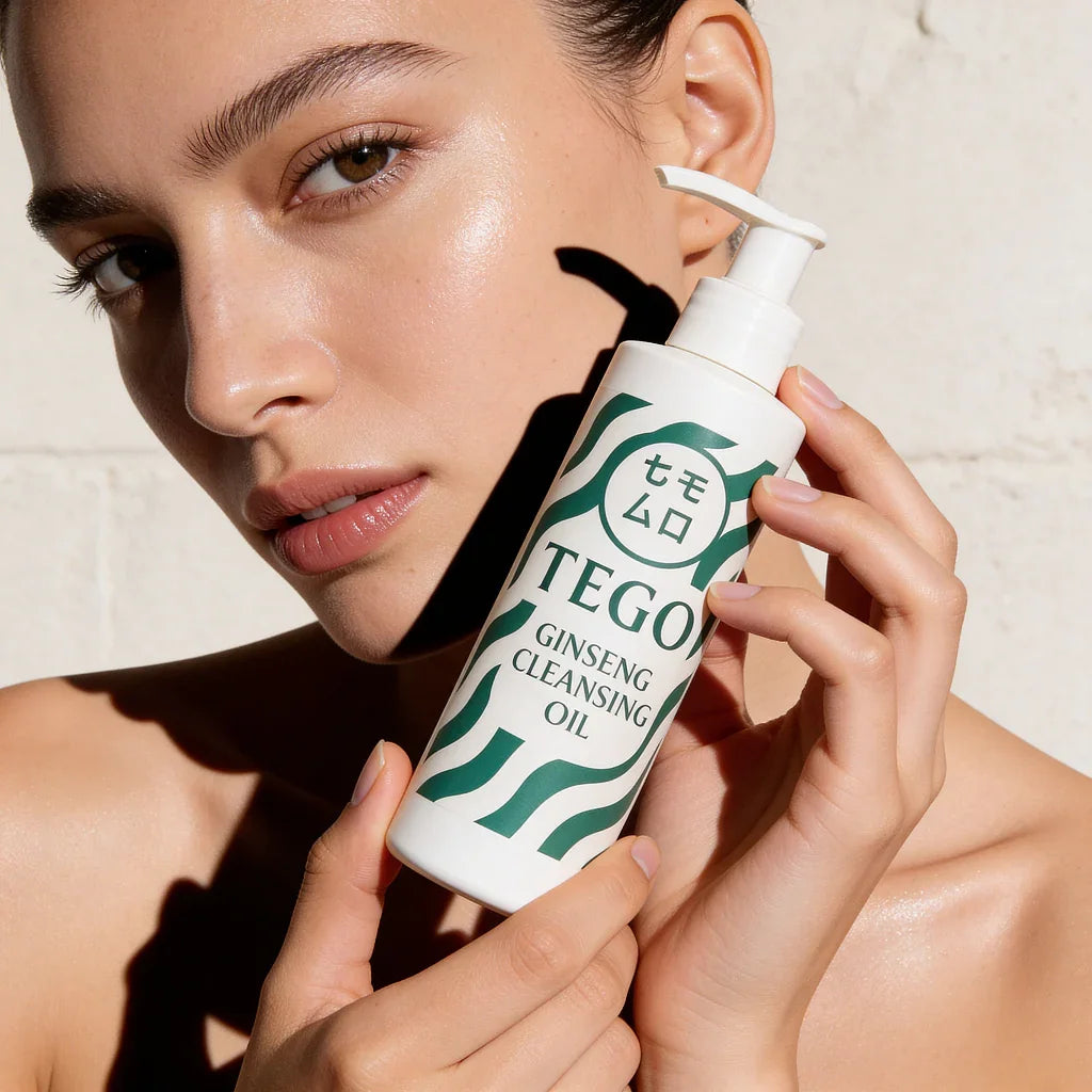 Kvinna med glowy hud håller flaska Tego Ginseng Cleansing Oil nära ansiktet.